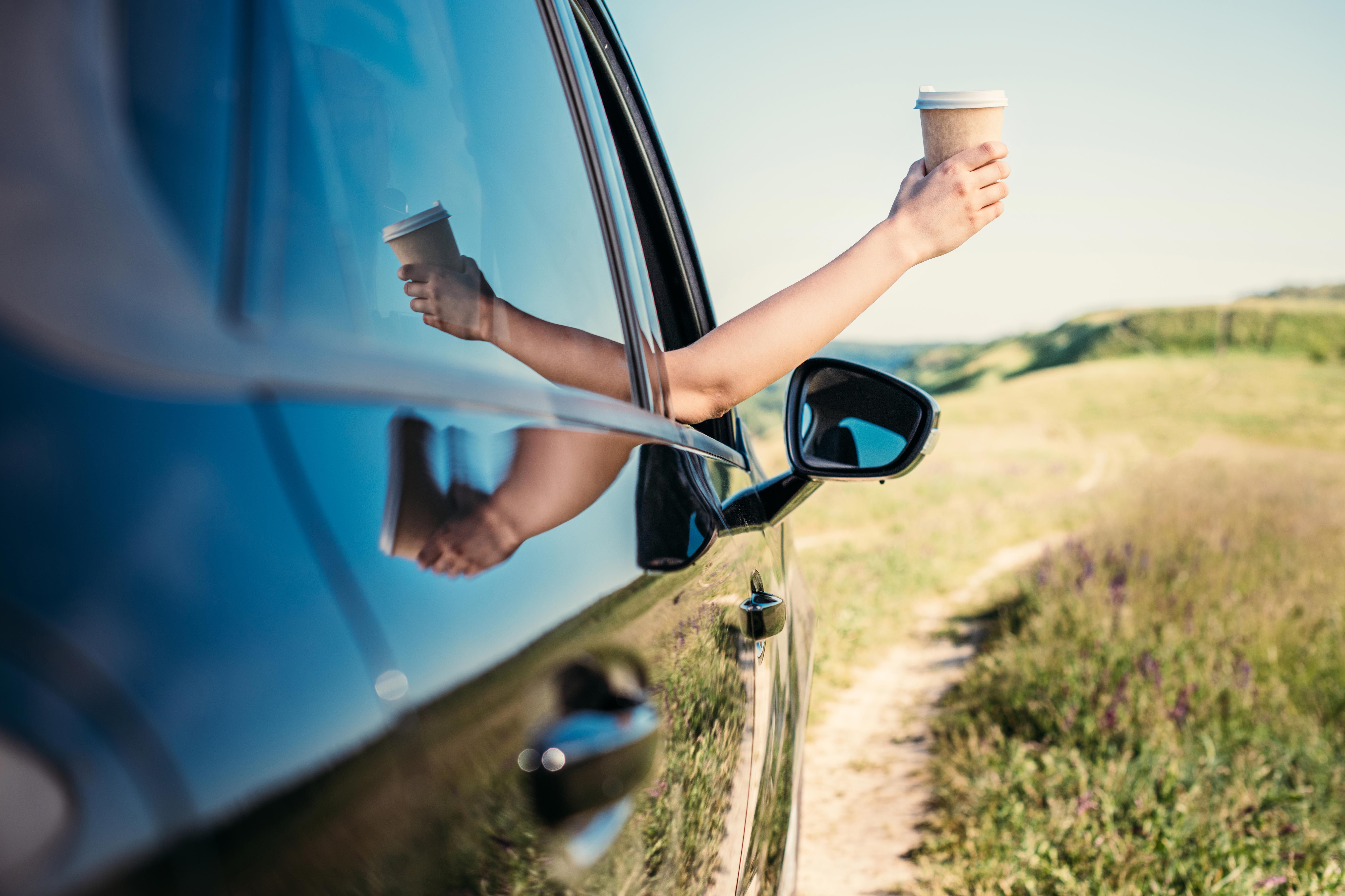 Person holding a coffee cup with hand outstretched from the car window
